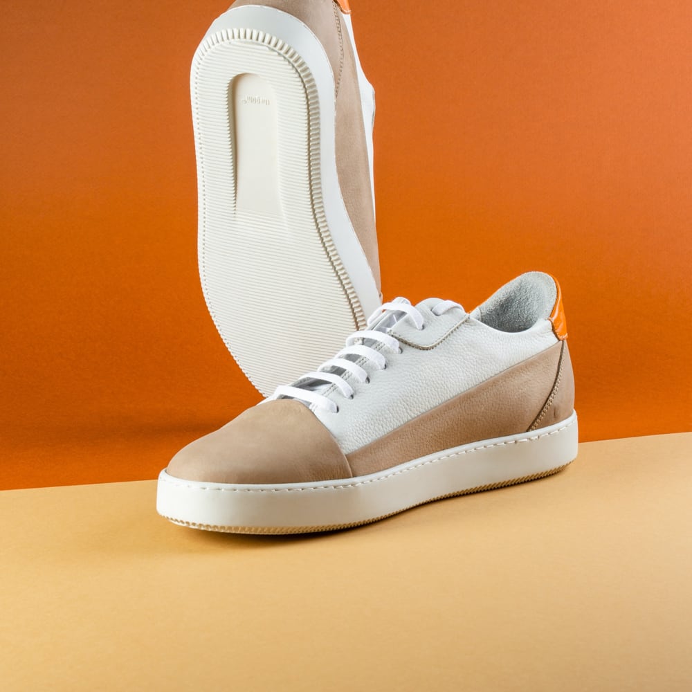Cream and tan low-profile sneakers against an orange backdrop